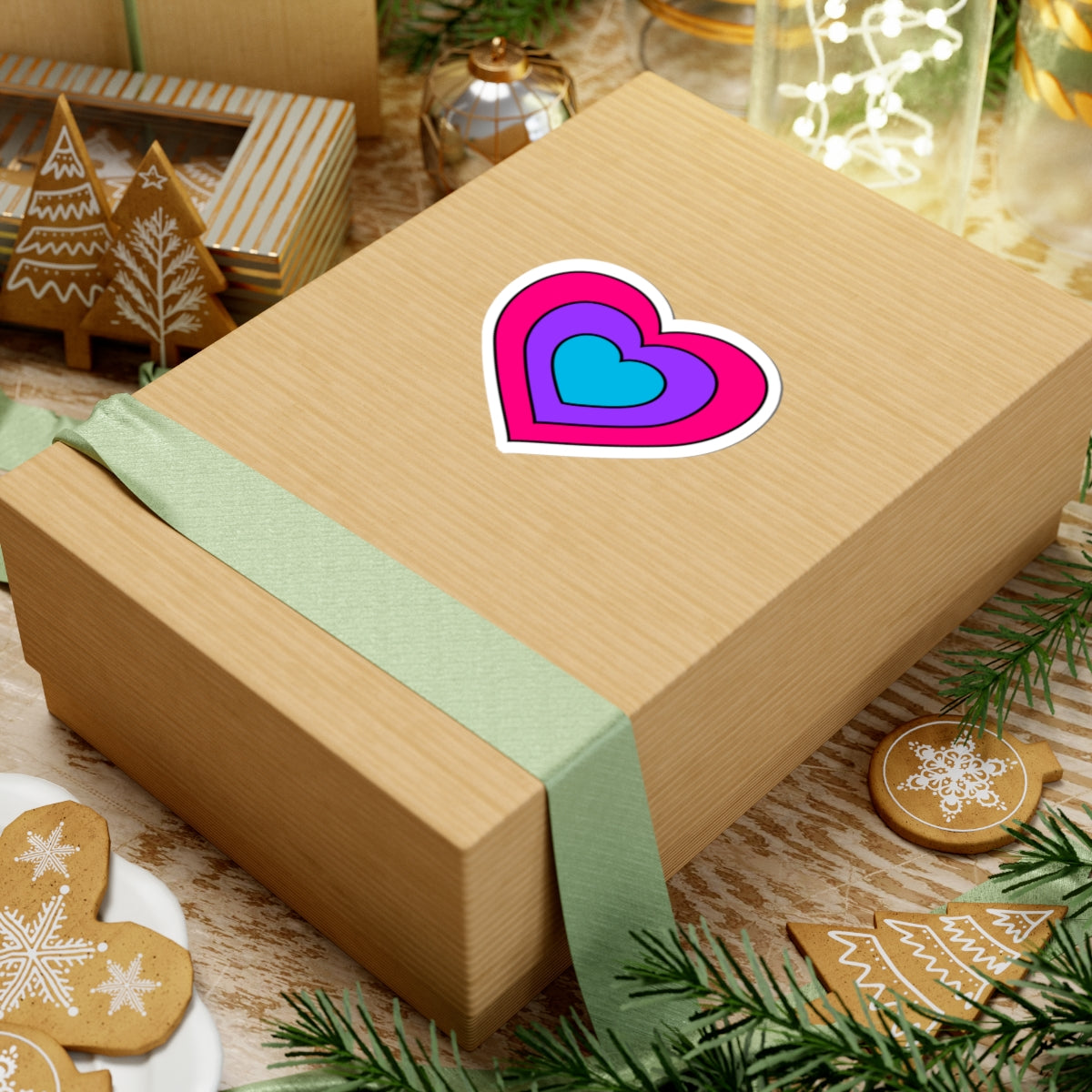 Gift box with a green ribbon on a festive background with cookies and Christmas decorations. Heart-shaped Androgyne pride sticker centered on the box.