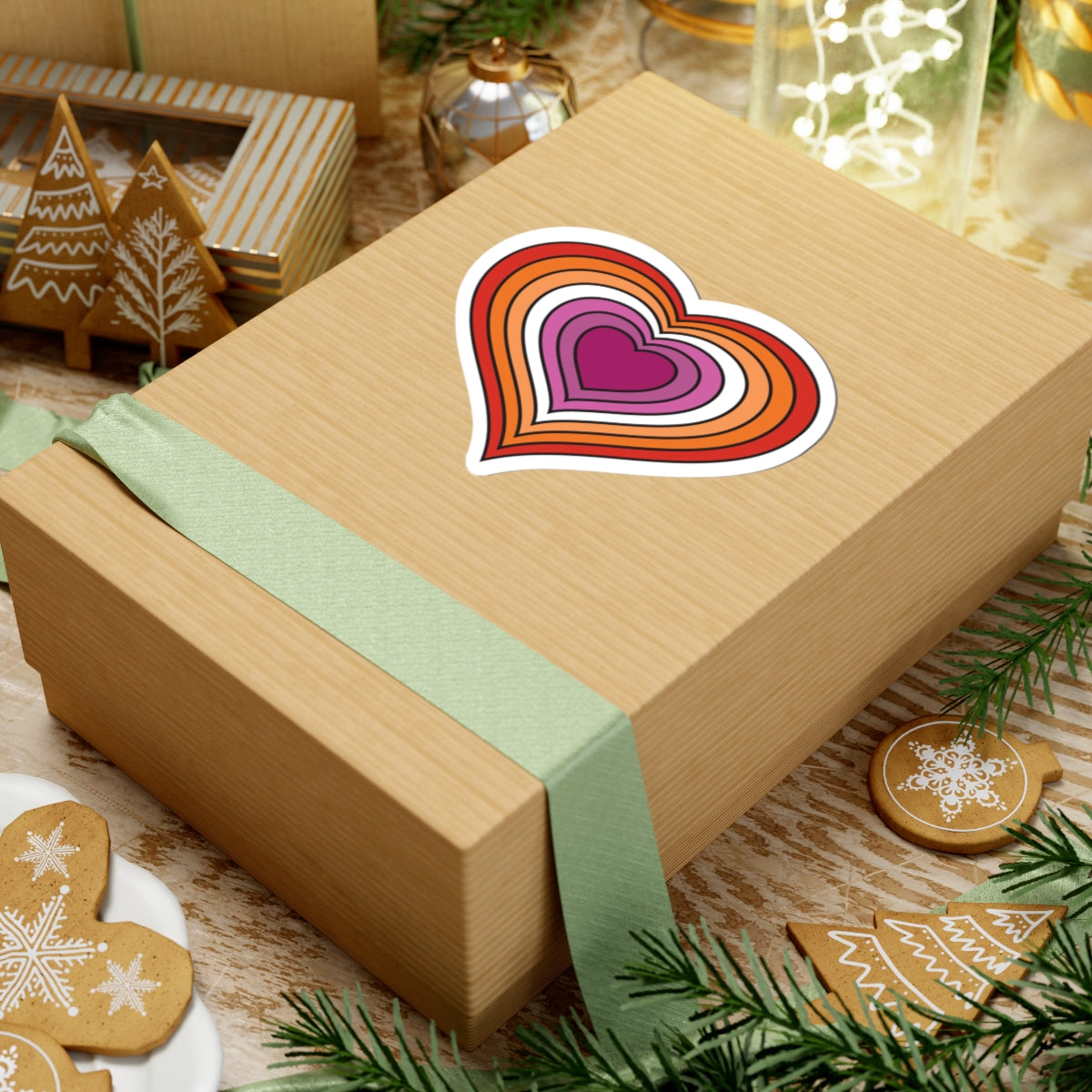 Gift box with a green ribbon on a festive table with cookies and decorations. Lesbian heart sticker centered on the box.