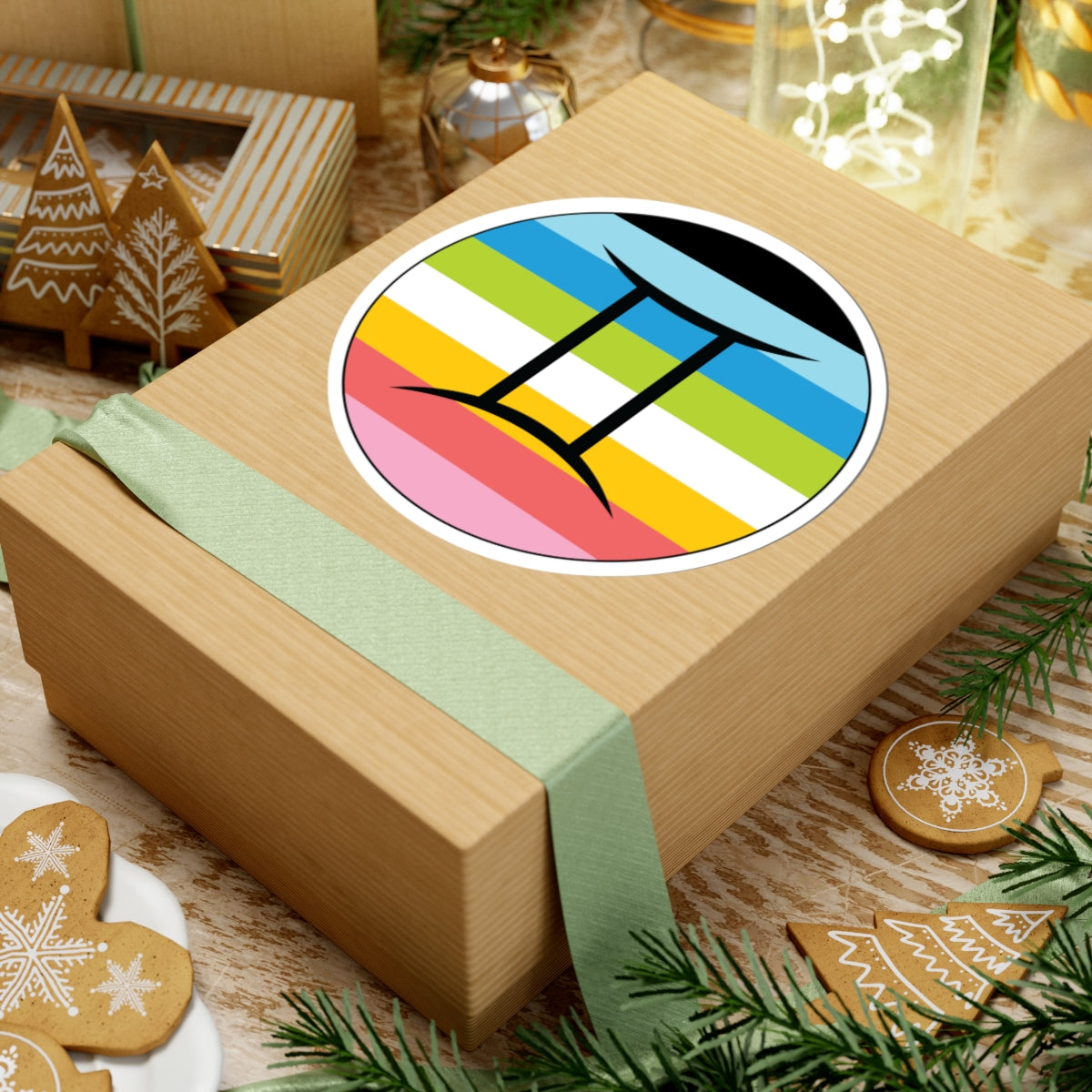 Gift box with a green ribbon on a festive background with cookies and Christmas decorations. Gemini Queer pride sticker centered on the box.