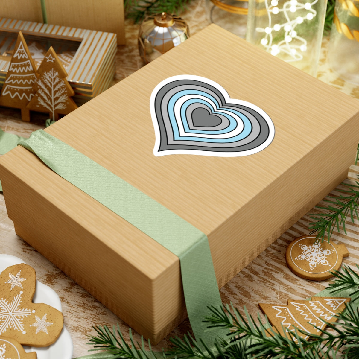 Gift box with a green ribbon on a festive background with cookies and Christmas decorations. Heart-shaped Demiboy pride sticker centered on the box.