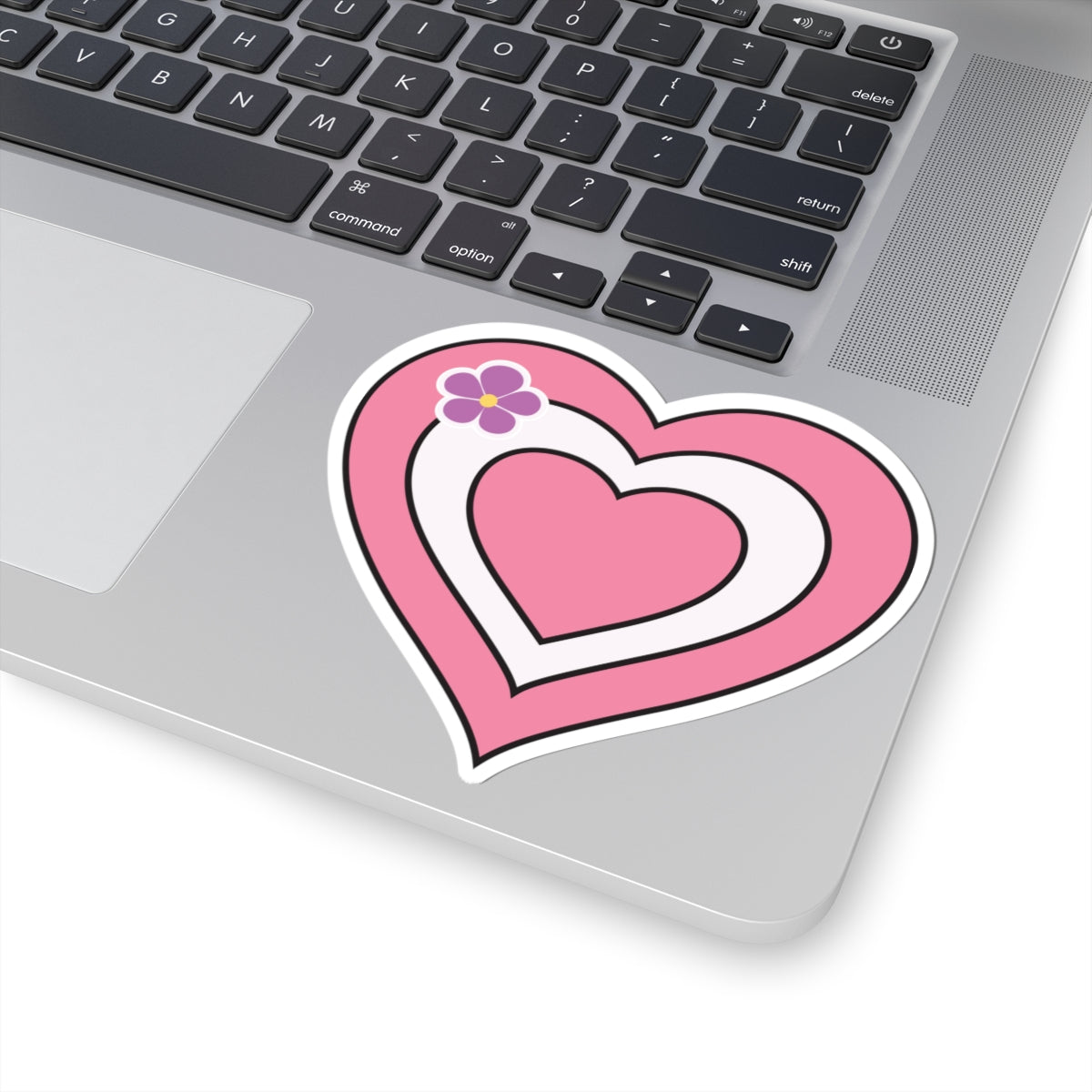 Close-up of the bottom right corner of a silver laptop featuring a 4 inch by 4 inch pride flag heart sticker in a Sapphic pride flag style applied to the surface.