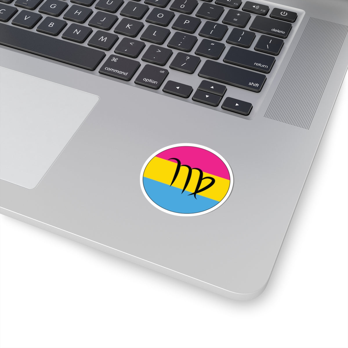 Close-up of the bottom right corner of a silver laptop featuring a 2 inch by 2 inch circular zodiac sticker with a centered Virgo glyph on a Pansexual pride flag style background applied to the surface.
