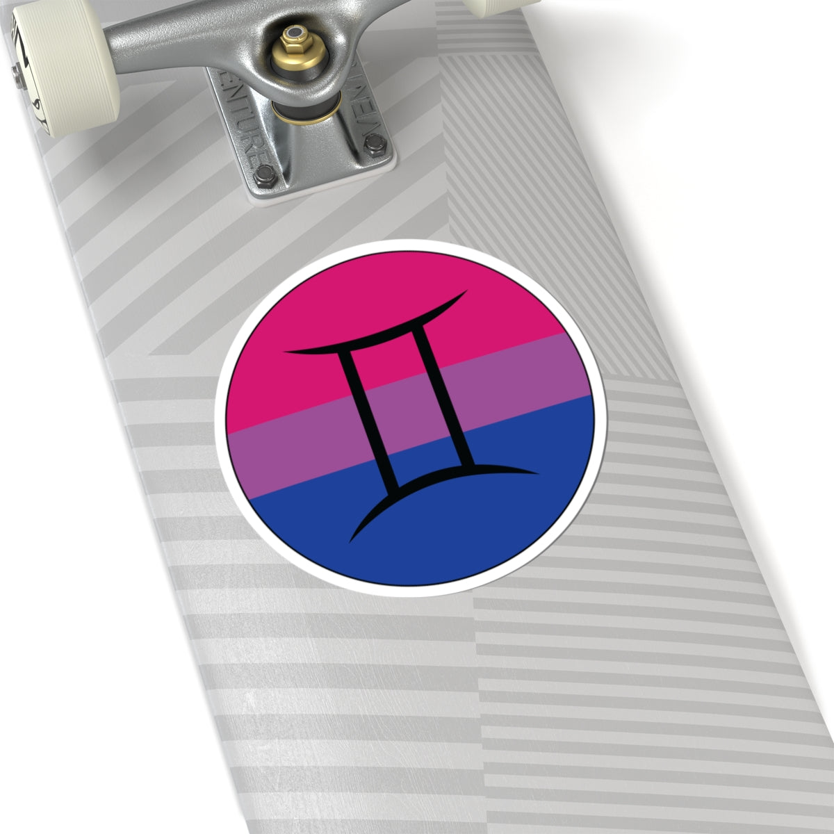 Close-up of the bottom of a silver skateboard featuring a 6 inch by 6 inch circular zodiac sticker with a centered Gemini glyph on a Bisexual pride flag style background applied to the surface.