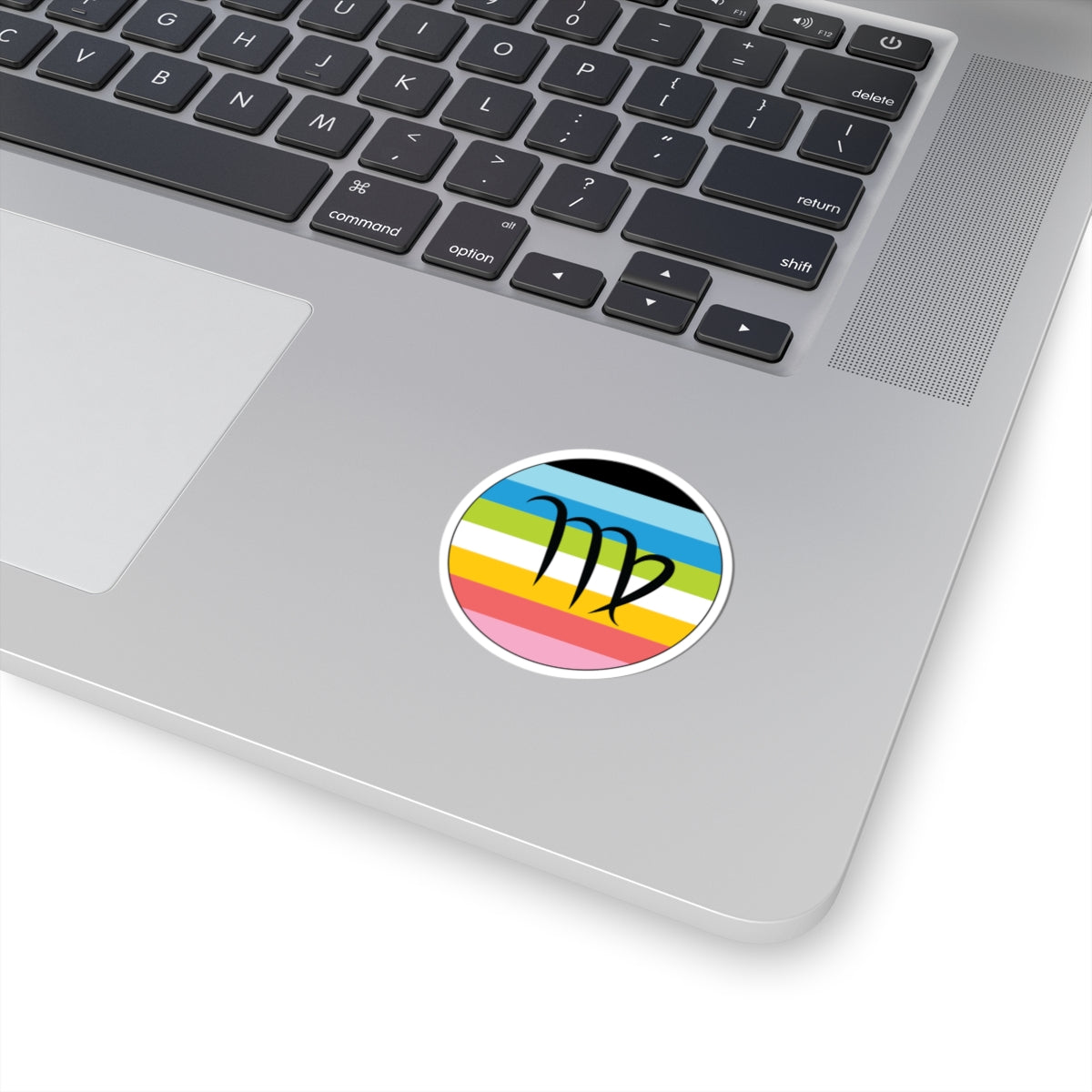 Close-up of the bottom right corner of a silver laptop featuring a 2 inch by 2 inch circular zodiac sticker with a centered Virgo glyph on a Queer pride flag style background applied to the surface.