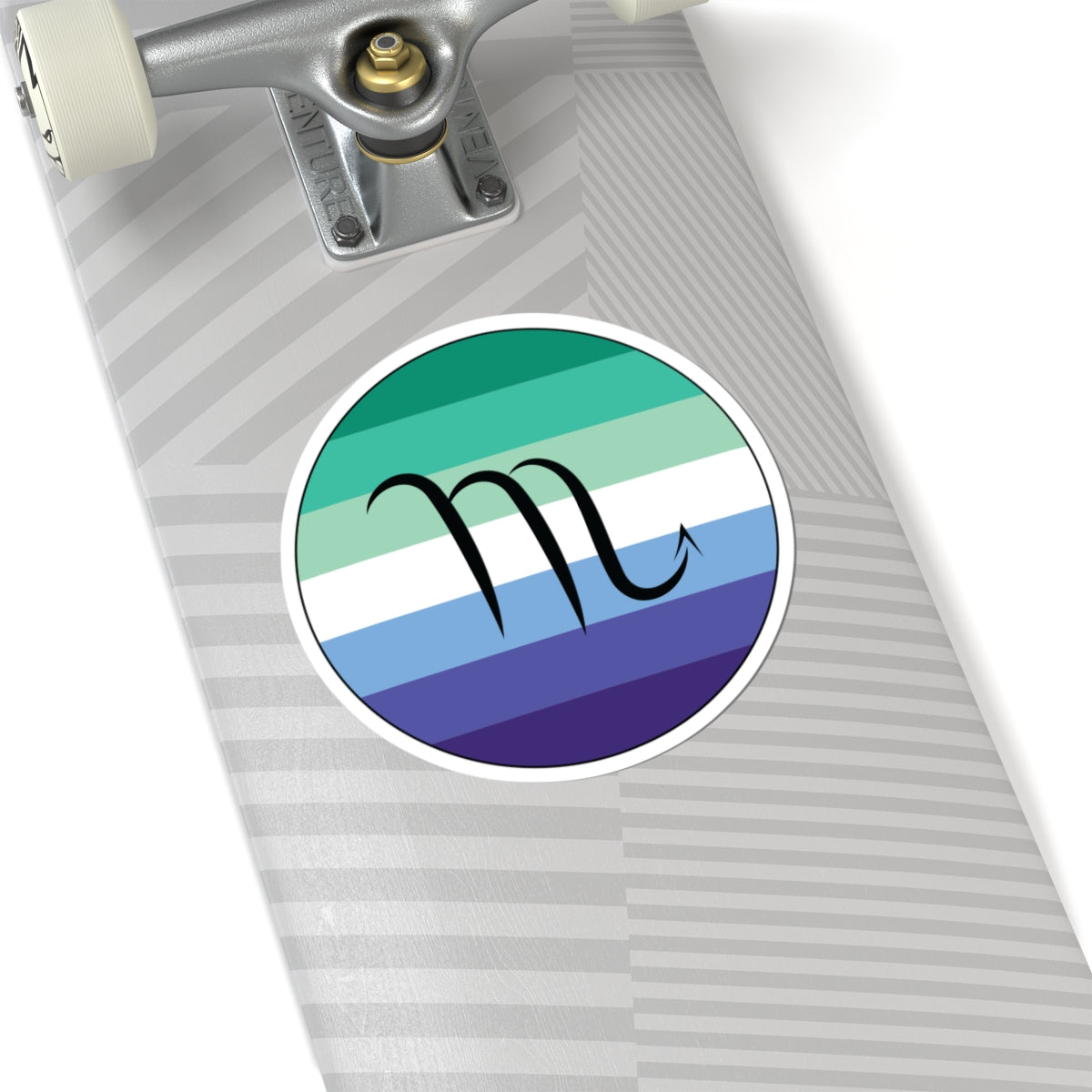 Close-up of the bottom of a silver skateboard featuring a 6 inch by 6 inch circular zodiac sticker with a centered Scorpio glyph on a Gay Men pride flag style background applied to the surface.