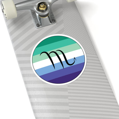 Close-up of the bottom of a silver skateboard featuring a 6 inch by 6 inch circular zodiac sticker with a centered Scorpio glyph on a Gay Men pride flag style background applied to the surface.