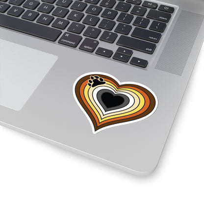 Close-up of the bottom right corner of a silver laptop featuring a 3 inch by 3 inch pride flag heart sticker in a Bear pride flag style applied to the surface.