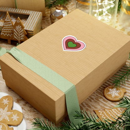 Gift box with a green ribbon on a festive background with cookies and Christmas decorations. Heart-shaped Gynesexual pride sticker centered on the box.