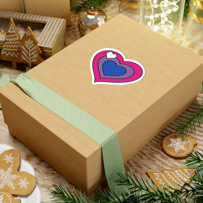 Gift box with a green ribbon on a festive background with cookies and Christmas decorations. Heart-shaped biromantic pride sticker centered on the box.