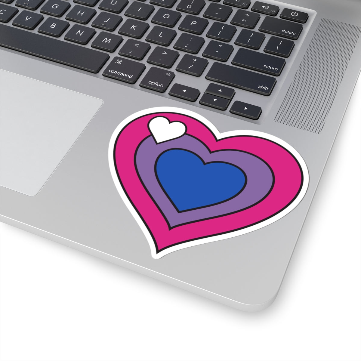 Close-up of the bottom right corner of a silver laptop featuring a 4 inch by 4 inch pride flag heart sticker in a Biromantic flag style applied to the surface.