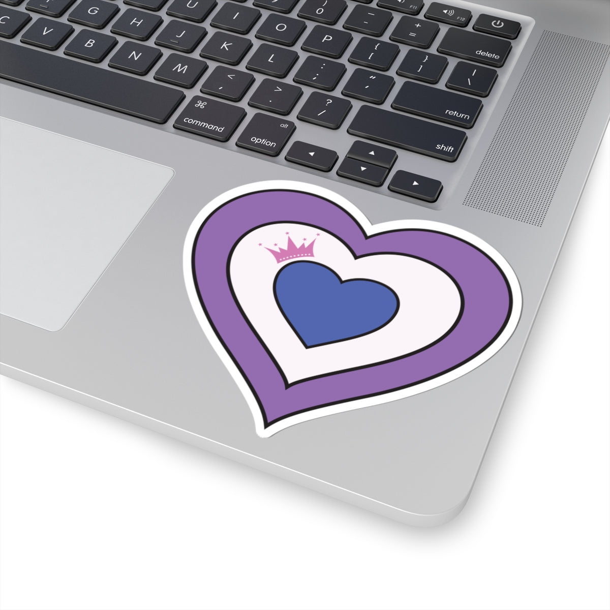 Close-up of the bottom right corner of a silver laptop featuring a 4 inches by 4 inches pride flag heart sticker in a Drag pride flag style applied to the surface.