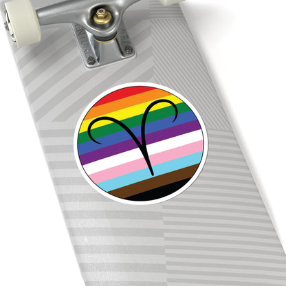 Close-up of the bottom of a silver skateboard featuring a 6 inch by 6 inch circular zodiac sticker with a centered Aires glyph on a progress pride flag style background applied to the surface.
