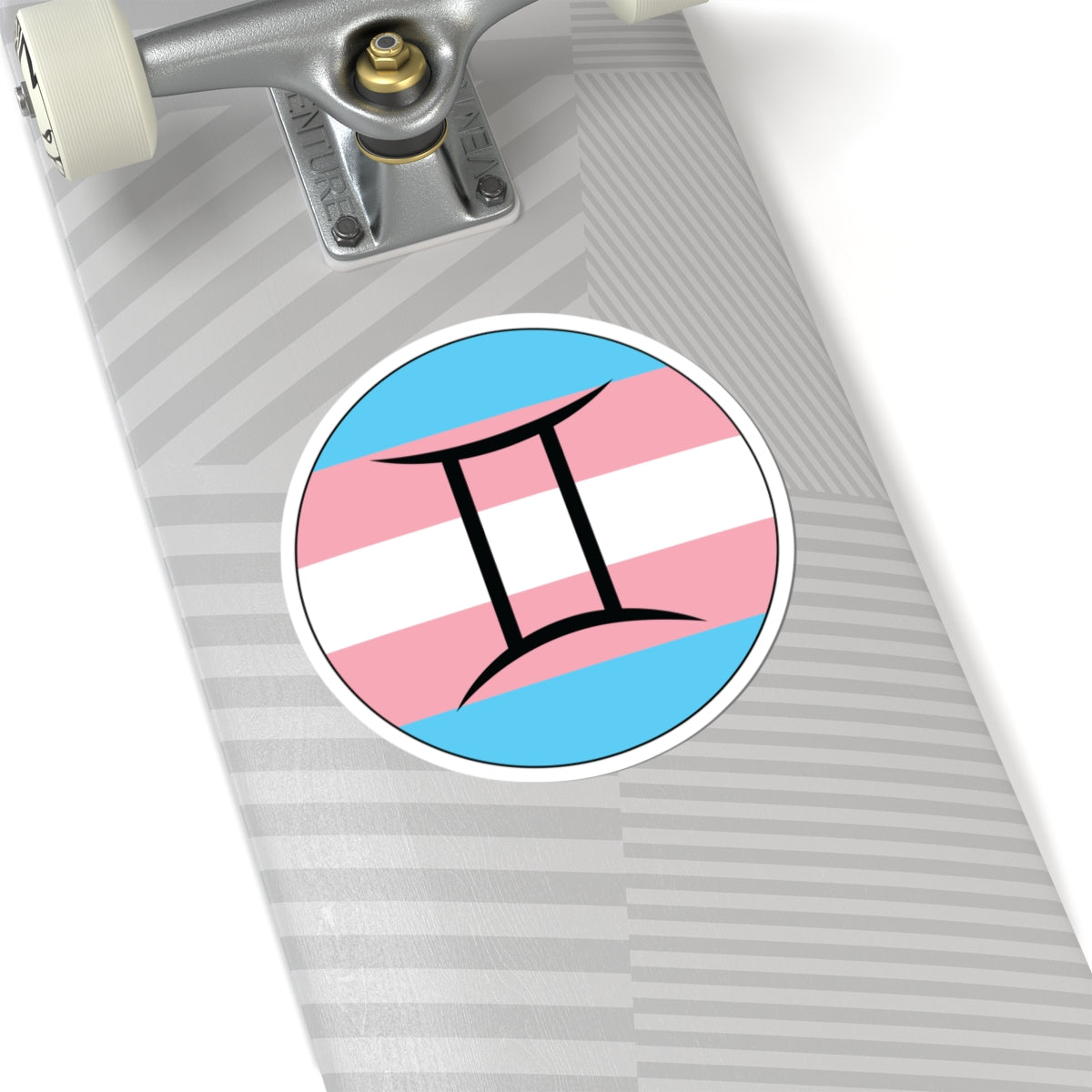 Close-up of the bottom of a silver skateboard featuring a 6 inch by 6 inch circular zodiac sticker with a centered Gemini glyph on a Transgender pride flag style background applied to the surface.