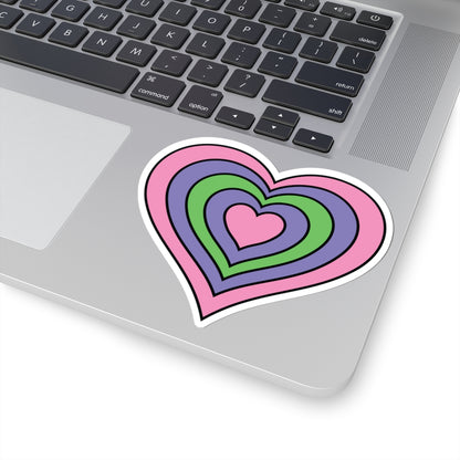 Close-up of the bottom right corner of a silver laptop featuring a 4 inch by 4 inch pride flag heart sticker in a Trigender flag style applied to the surface.