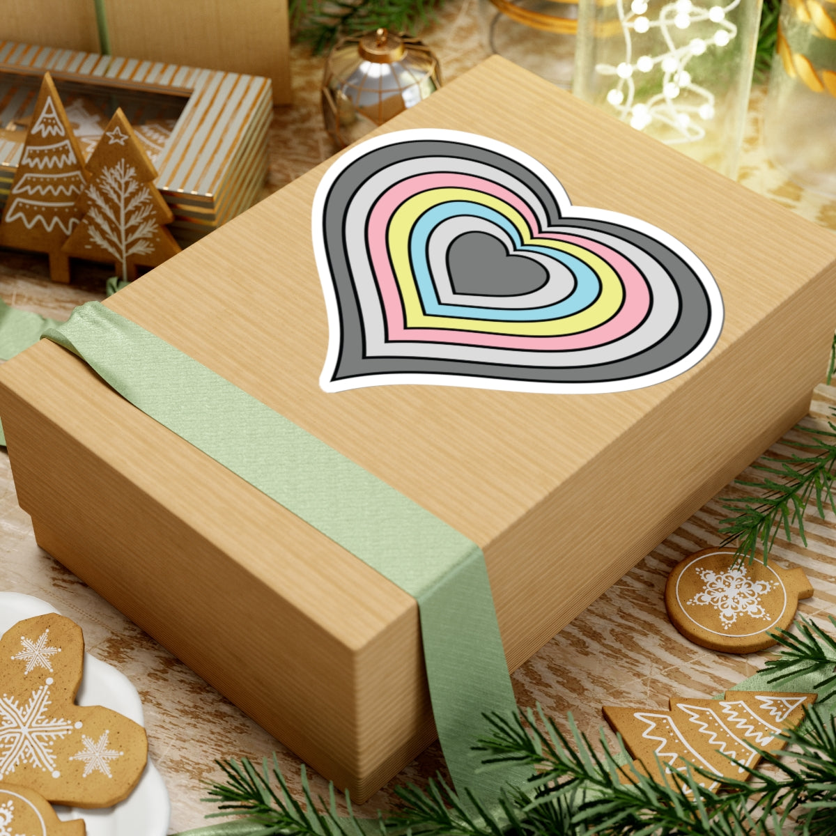 Gift box with a green ribbon on a festive background with cookies and Christmas decorations. Heart-shaped Demiflux pride sticker centered on the box.