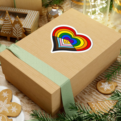 Gift box with a green ribbon on a festive background with cookies and Christmas decorations. Heart-shaped Intersex-inclusive progress pride sticker centered on the box.