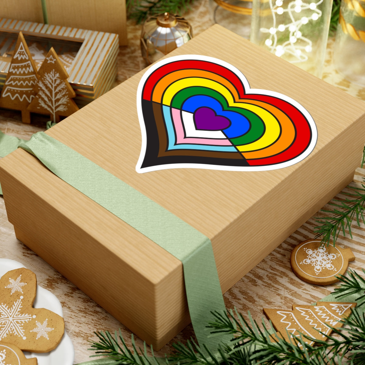 Gift box with a green ribbon on a festive background with cookies and Christmas decorations. Heart-shaped progress pride sticker centered on the box.