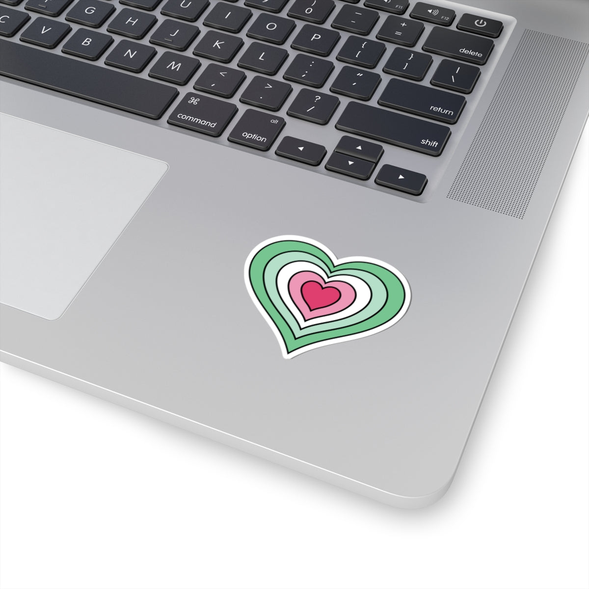 Close-up of the bottom right corner of a silver laptop featuring a 2 inch by 2 inch pride flag heart sticker in an Abrosexual flag style applied to the surface.