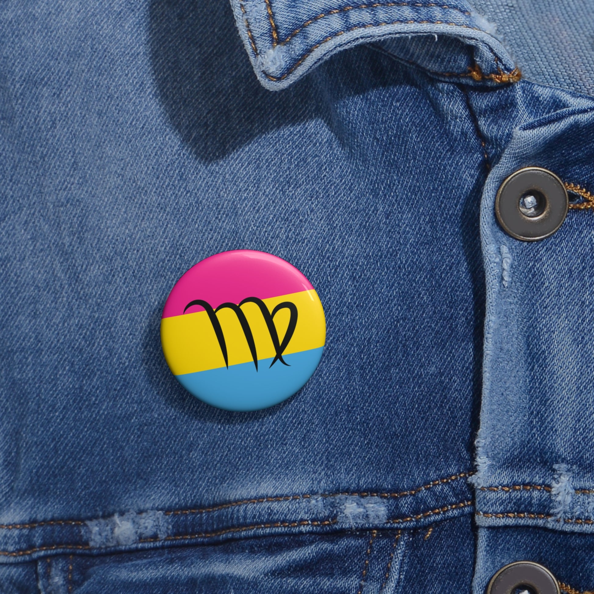 Close-up of a white circular pride button featuring the Virgo zodiac glyph centered over a Pansexual pride flag background in pink, yellow, and blue, attached to a blue denim jacket at the right chest with the button clearly visible.