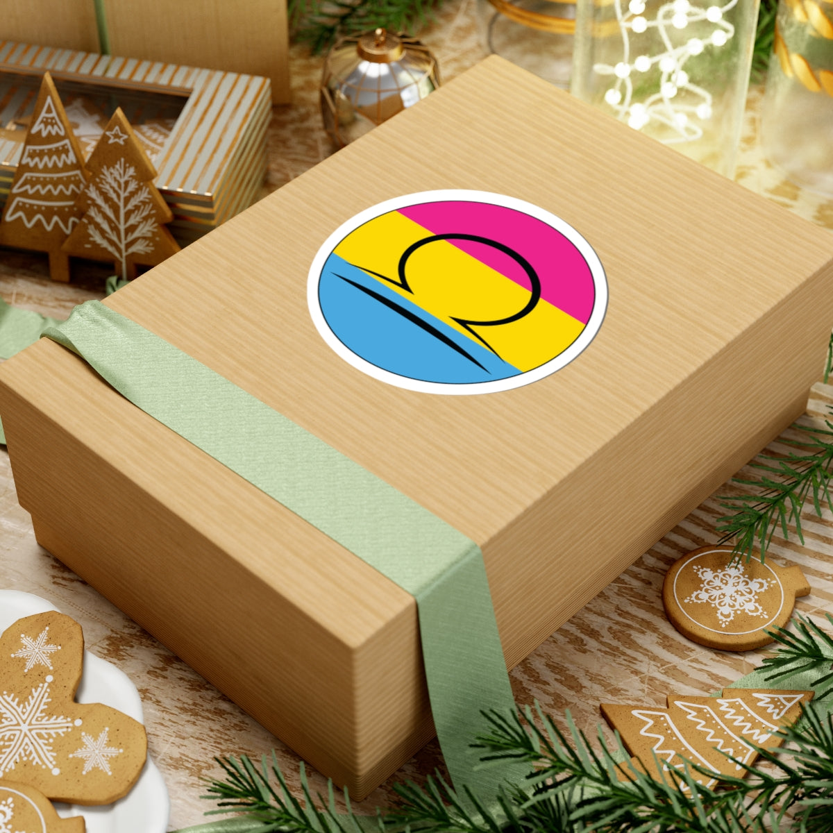 Gift box with a green ribbon on a festive background with cookies and Christmas decorations. Libra Pansexual pride sticker centered on the box.