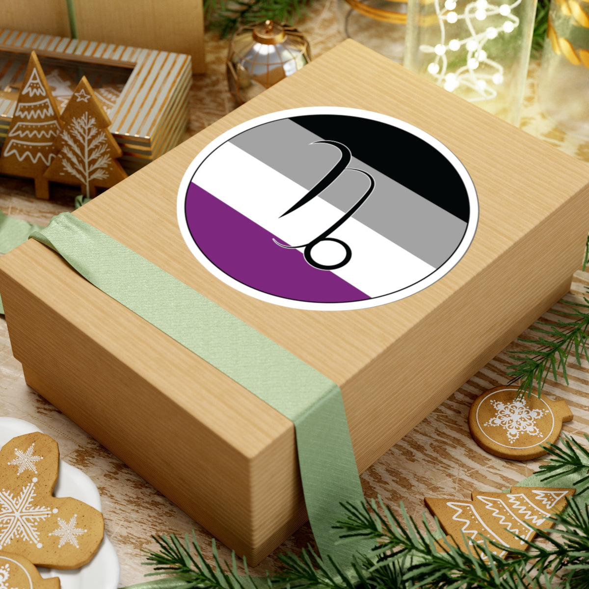 Gift box with a green ribbon on a festive background with cookies and Christmas decorations. Capricorn Asexual pride sticker centered on the box.