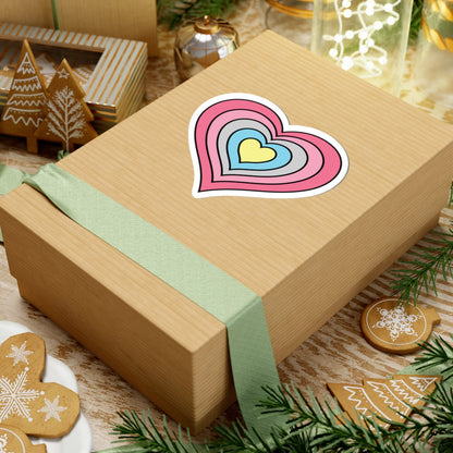 Gift box with a green ribbon on a festive background with cookies and Christmas decorations. Heart-shaped Genderflux pride sticker centered on the box.