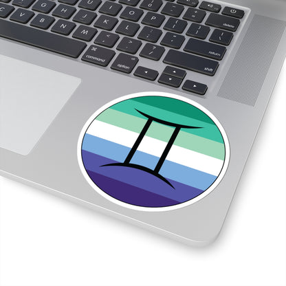 Close-up of the bottom right corner of a silver laptop featuring a 4 inch by 4 inch circular zodiac sticker with a centered Gemini glyph on a Gay Men pride flag style background applied to the surface.