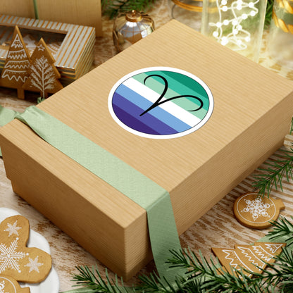 Gift box with a green ribbon on a festive background with cookies and Christmas decorations. Aires Gay Men pride sticker centered on the box.