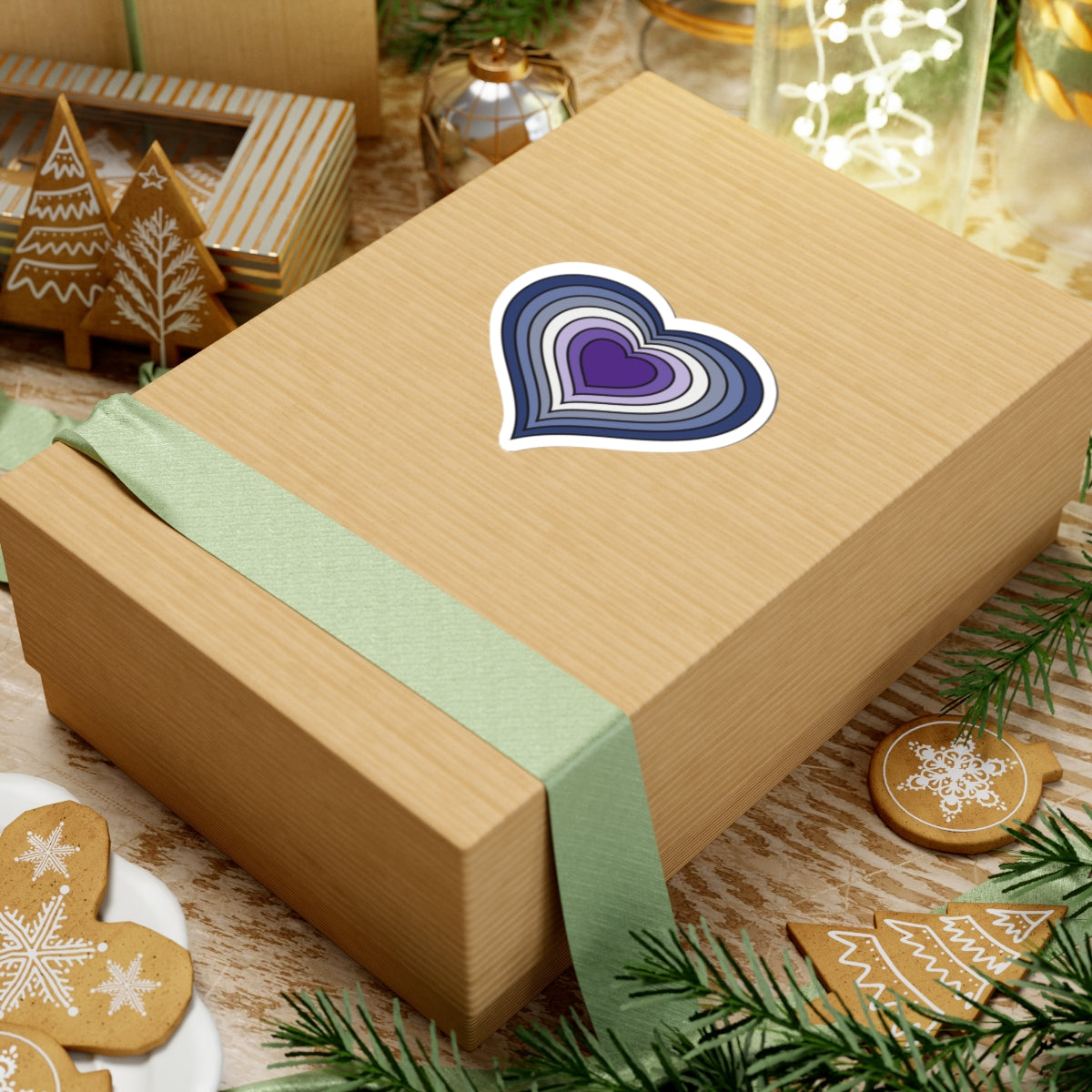 Gift box with a green ribbon on a festive background with cookies and Christmas decorations. Purple Butch pride heart sticker centered on the box.