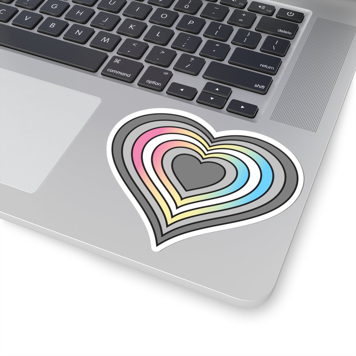 Close-up of the bottom right corner of a silver laptop featuring a 4 inch by 4 inch pride flag heart sticker in a Demifluid flag style applied to the surface.
