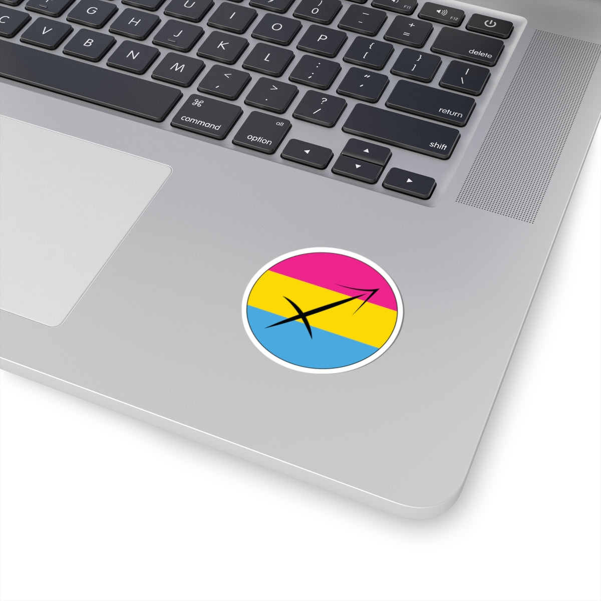 Close-up of the bottom right corner of a silver laptop featuring a 2 inch by 2 inch circular zodiac sticker with a centered Sagittarius glyph on a Pansexual pride flag style background applied to the surface.