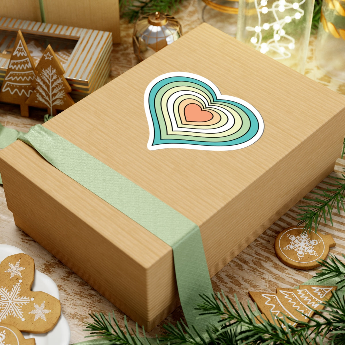 Gift box with a green ribbon on a festive background with cookies and Christmas decorations. Heart-shaped Genderfloren pride sticker centered on the box.