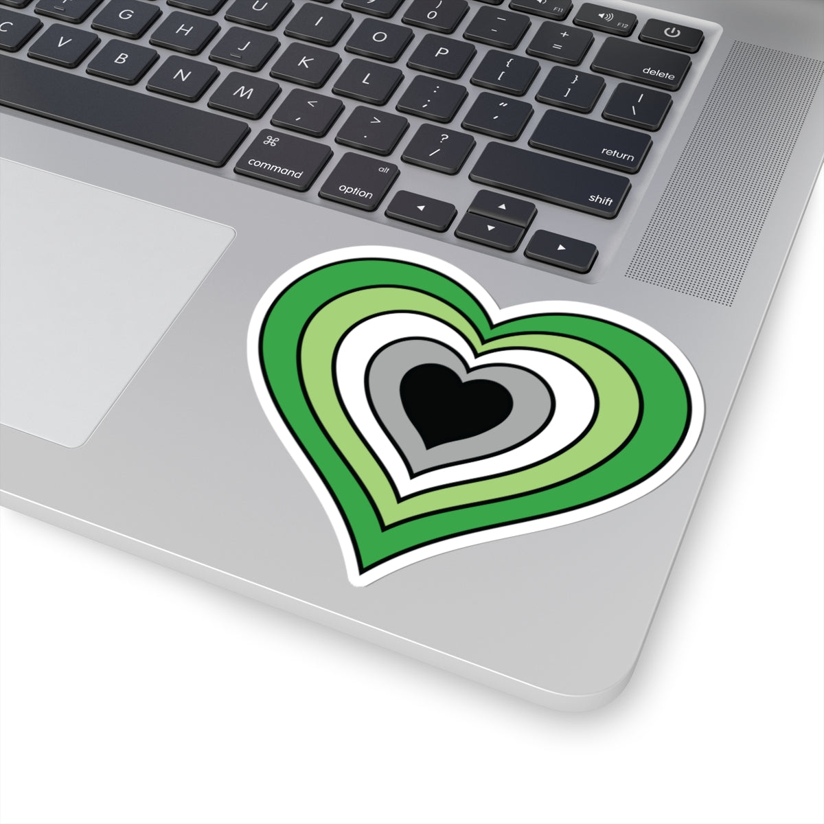 Close-up of the bottom right corner of a silver laptop featuring a 4 inch by 4 inch pride flag heart sticker in an Aromantic flag style applied to the surface.
