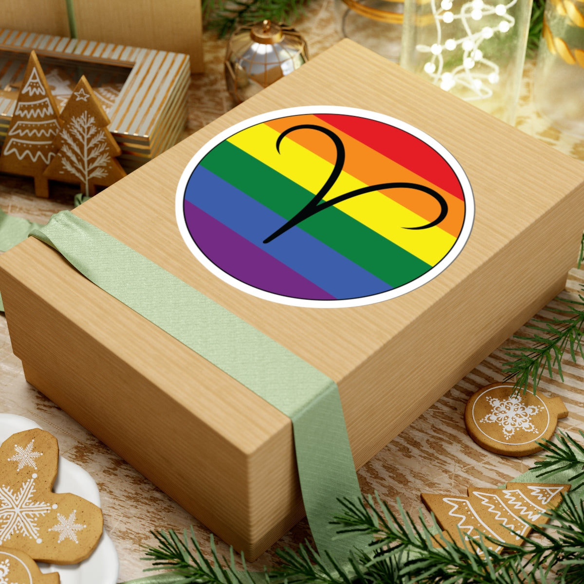 Gift box with a green ribbon on a festive background with cookies and Christmas decorations. Aires Rainbow pride sticker centered on the box.