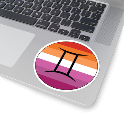 Close-up of the bottom right corner of a silver laptop featuring a 4 inch by 4 inch circular zodiac sticker with a centered Gemini glyph on a Lesbian pride flag style background applied to the surface.