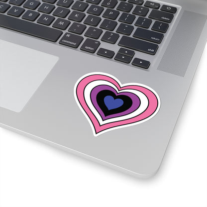 Close-up of the bottom right corner of a silver laptop featuring a 3 inch by 3 inch pride flag heart sticker in a Genderfluid flag style applied to the surface.