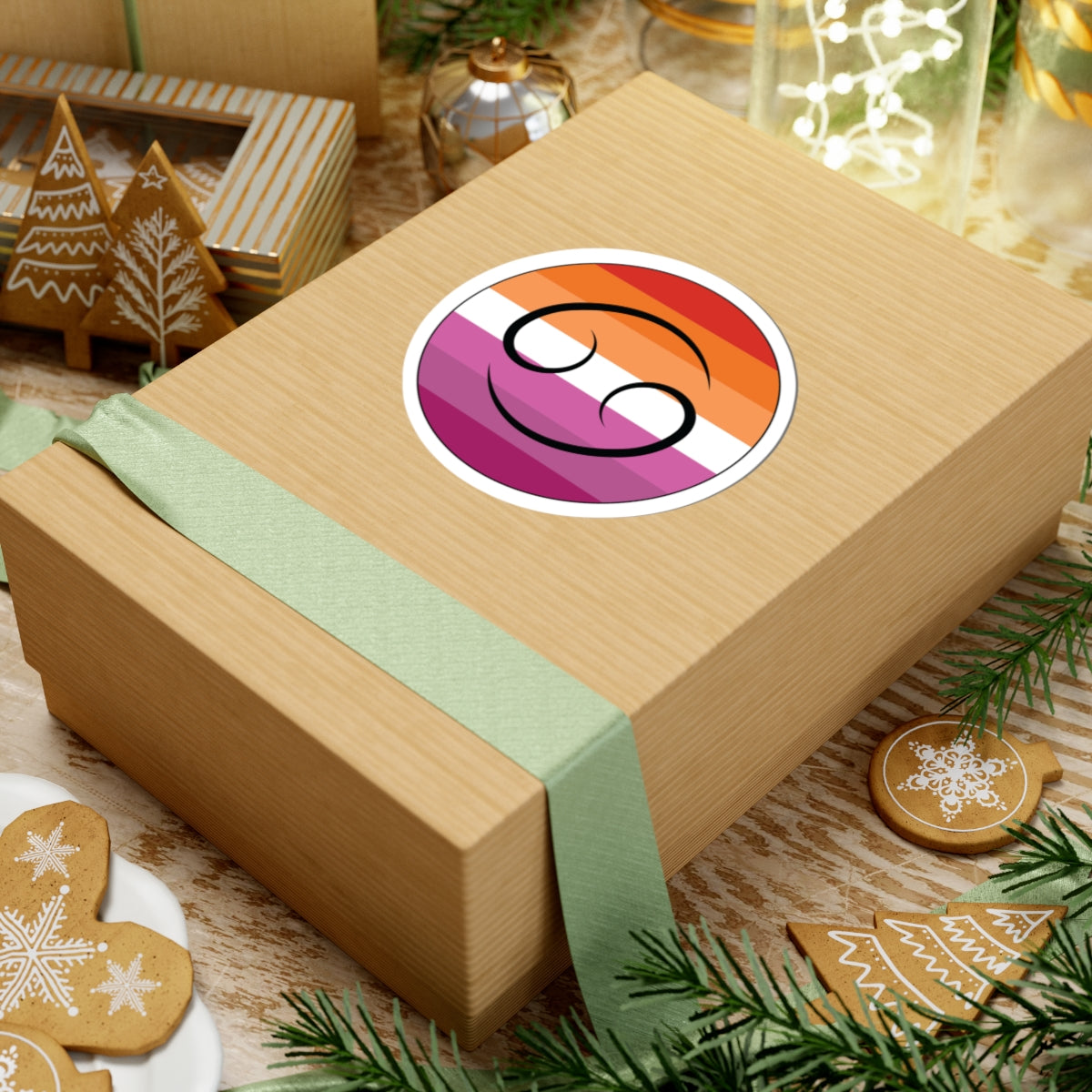 Gift box with a green ribbon on a festive background with cookies and Christmas decorations. Cancer Lesbian pride sticker centered on the box.