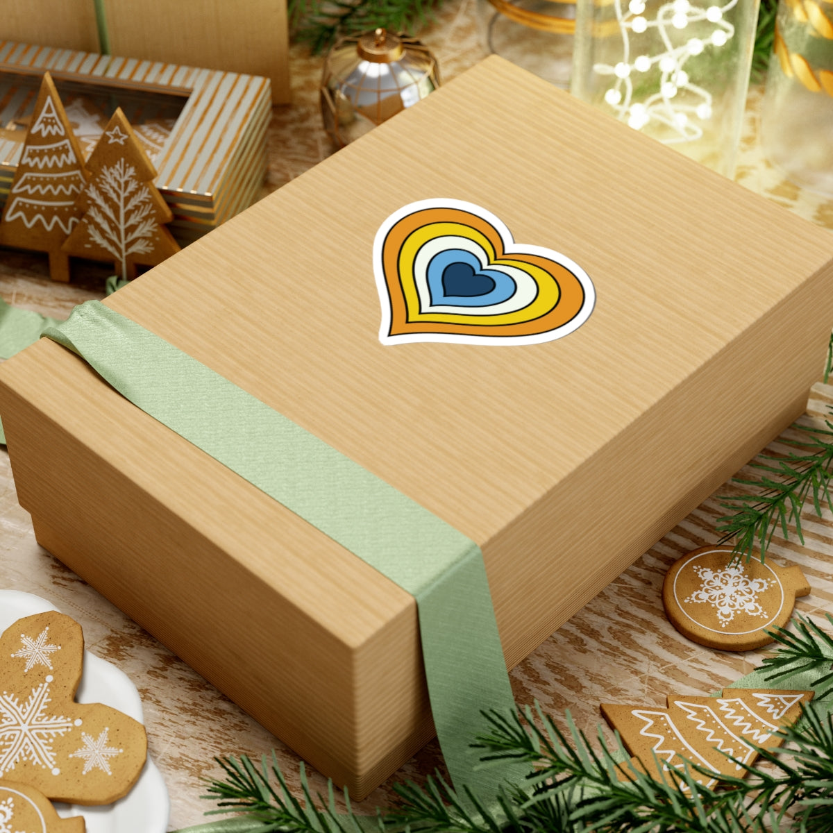Gift box with a green ribbon on a festive background with cookies and Christmas decorations. Heart-shaped Aroace pride sticker centered on the box.