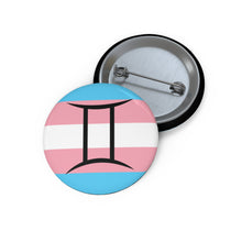 Front and back view of a circular transgender pride flag button featuring the Gemini zodiac symbol in black centered on the front.