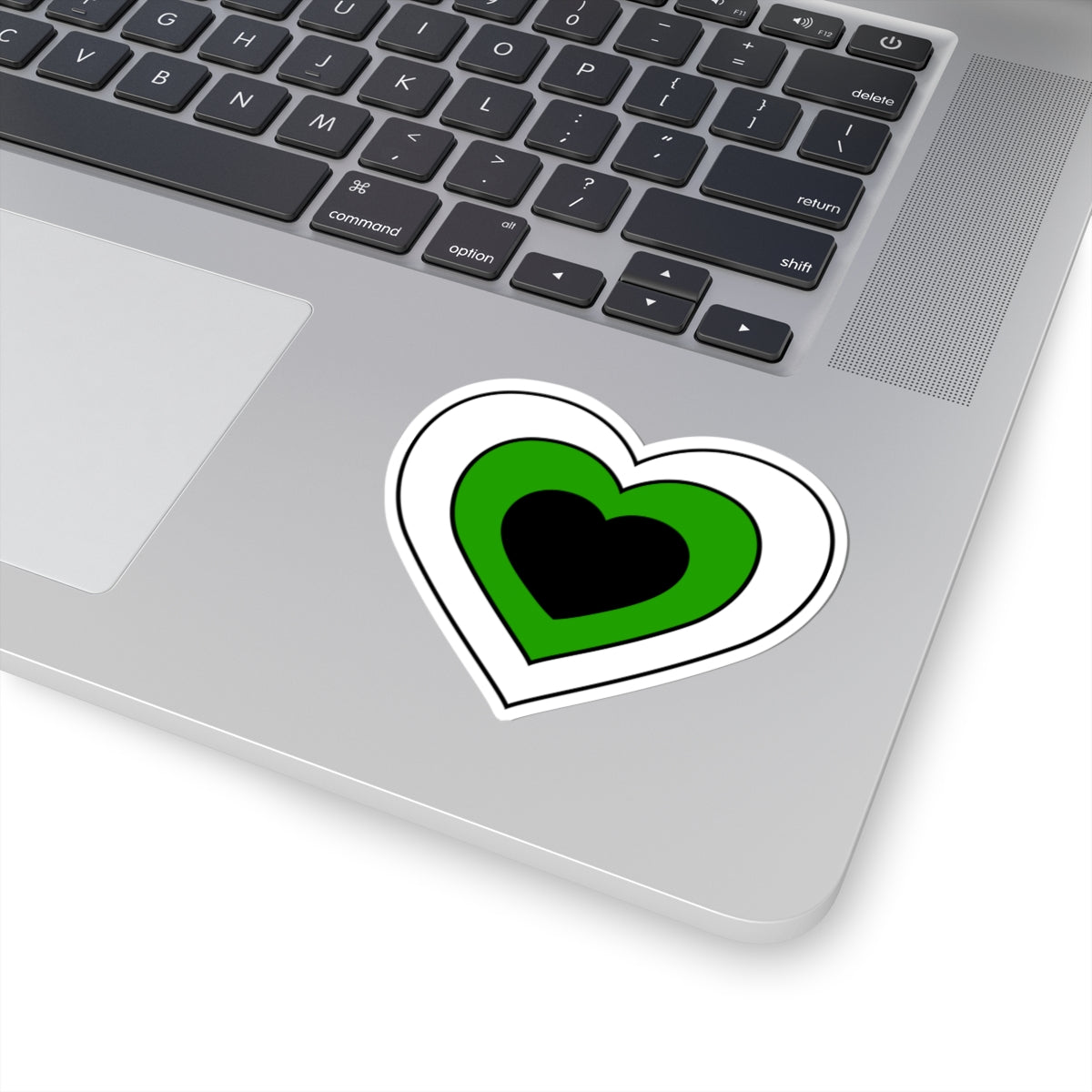 Close-up of the bottom right corner of a silver laptop featuring a 3 inch by 3 inch pride flag heart sticker in a Neutrois flag style applied to the surface.