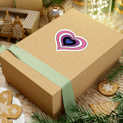 Gift box with a green ribbon on a festive background with cookies and Christmas decorations. Heart-shaped Genderfluid pride sticker centered on the box.