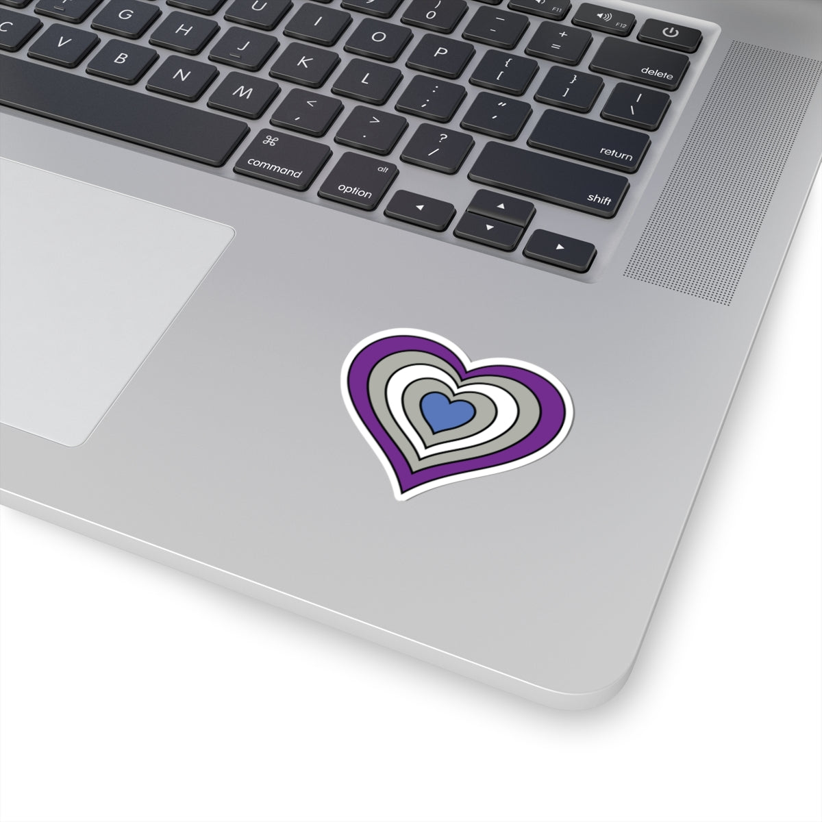 Close-up of the bottom right corner of a silver laptop featuring a 2 inch by 2 inch pride flag heart sticker in a Greysexual flag style applied to the surface.