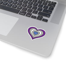 Close-up of the bottom right corner of a silver laptop featuring a 2 inch by 2 inch pride flag heart sticker in a Greysexual flag style applied to the surface.