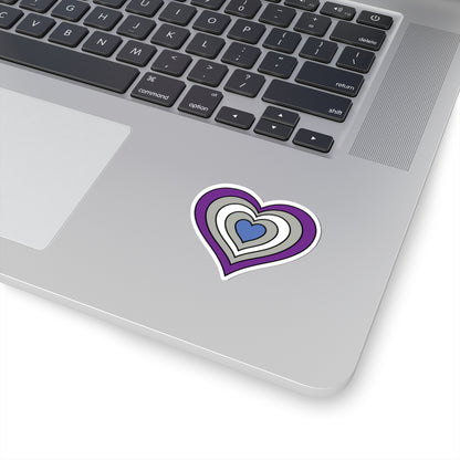 Close-up of the bottom right corner of a silver laptop featuring a 2 inch by 2 inch pride flag heart sticker in a Greysexual flag style applied to the surface.