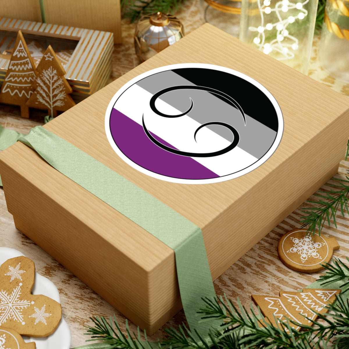 Gift box with a green ribbon on a festive background with cookies and Christmas decorations. Cancer Asexual pride sticker centered on the box.