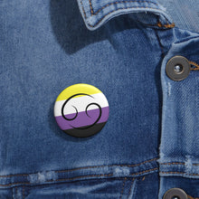 Close-up of a white circular pride button featuring the Cancer zodiac glyph centered over a nonbinary pride flag background in yellow, white, purple, and black, attached to a blue denim jacket at the right chest with the button clearly visible.