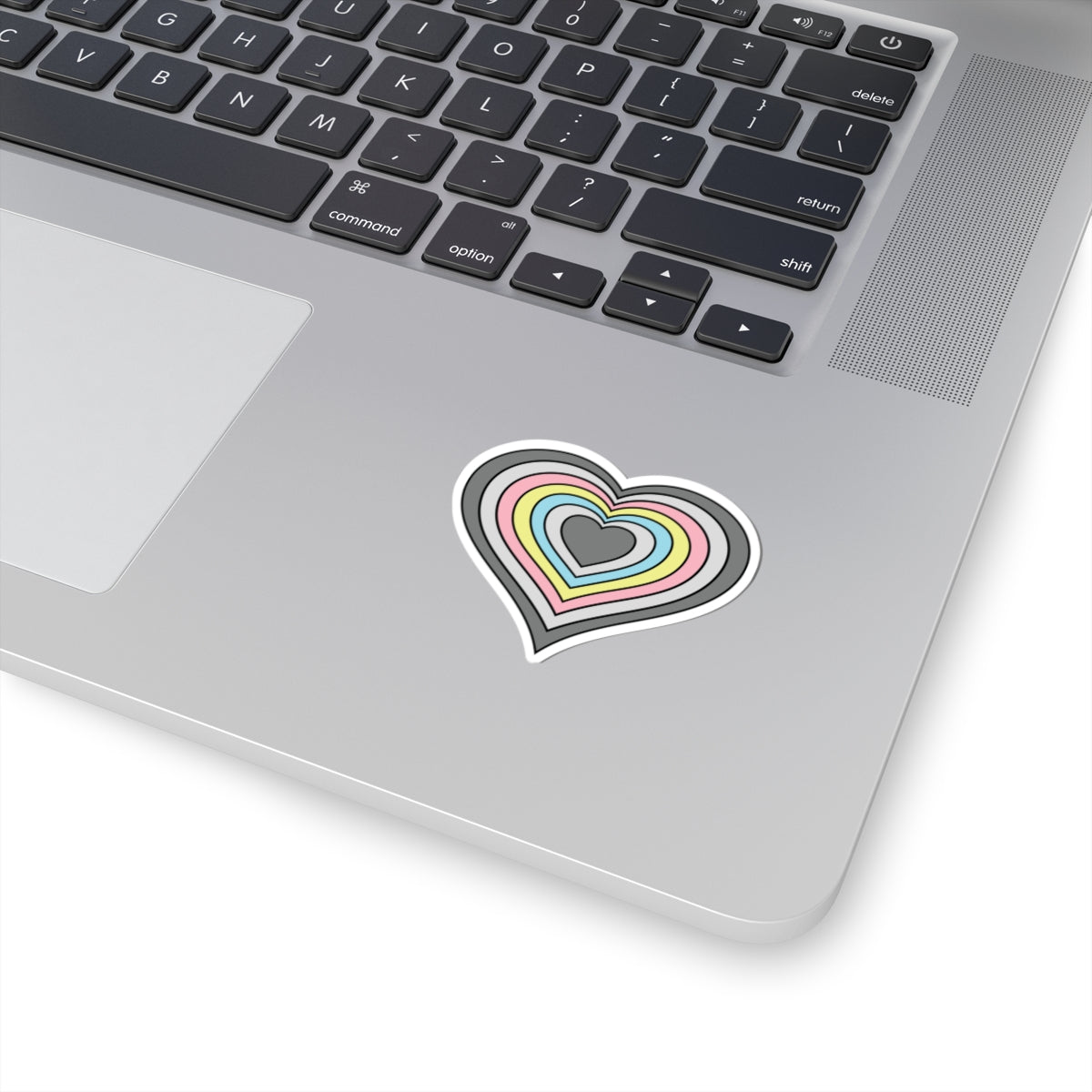 Close-up of the bottom right corner of a silver laptop featuring a 2 inch by 2 inch pride flag heart sticker in a Demiflux flag style applied to the surface.