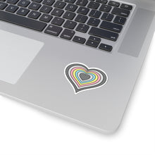 Close-up of the bottom right corner of a silver laptop featuring a 2 inch by 2 inch pride flag heart sticker in a Demiflux flag style applied to the surface.