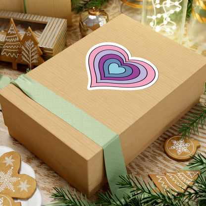 Gift box with a green ribbon on a festive background with cookies and Christmas decorations. Heart-shaped Omnigender pride sticker centered on the box.