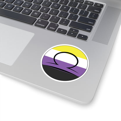Close-up of the bottom right corner of a silver laptop featuring a 3 inch by 3 inch circular zodiac sticker with a centered Libra glyph on a Nonbinary pride flag style background applied to the surface.